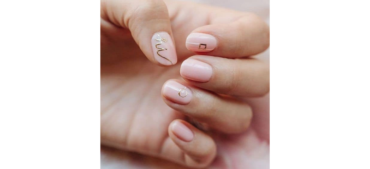 Ongles nudes avec des détails dorés et un mot imprimé
